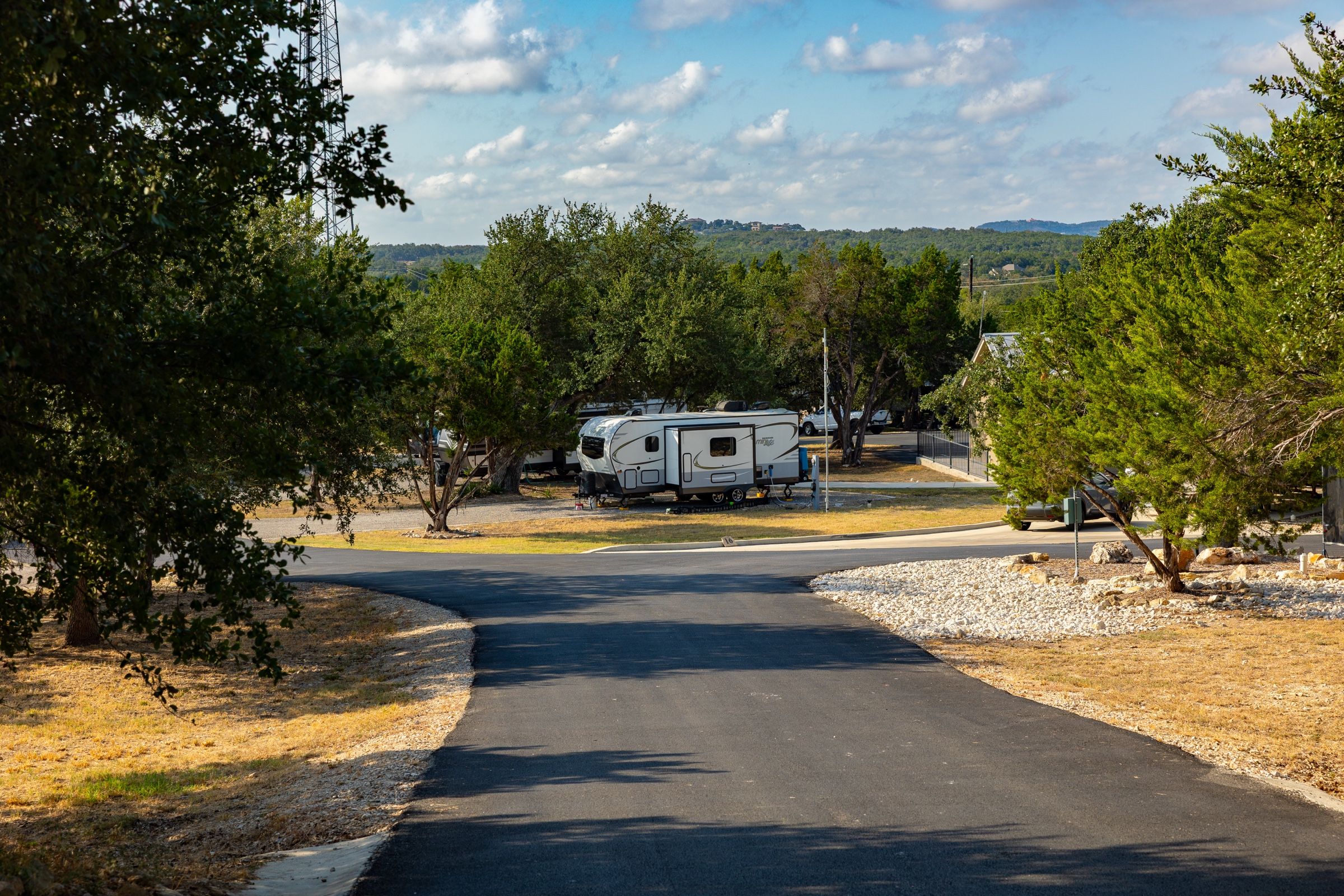 Paved drive in the park past a travel trailer, with Hill Country ridges beyond